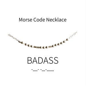 May include: A silver necklace with beads and a silver chain. The necklace spells out the word "BADASS" in Morse code. The Morse code for "BADASS" is shown below the necklace.