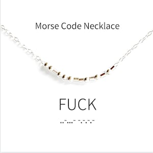 Op de afbeelding: Een zilveren ketting met een ketting en kleine kralen die het woord "FUCK" in morsecode spellen. De morsecode staat onder het woord.