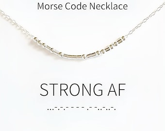 Può includere: Una collana a catena color argento con una serie di piccole perline metalliche e distanziatori cilindrici disposti in un motivo a codice Morse. Il testo 'Morse Code Necklace' e 'STRONG AF' con i punti e le linee del codice sono visibili.