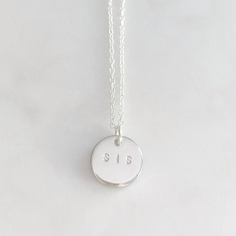 May include: A silver necklace with a round pendant that says "SIS" on it.