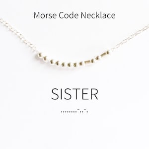 May include: A silver necklace with small beads that spell out the word "SISTER" in Morse code. The Morse code for "SISTER" is shown below the necklace.
