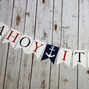 Puede incluir: Una pancarta de Ahoy It's a Boy con letras rojas y azules y anclas en banderines blancos. La pancarta est&aacute; enhebrada en un fondo blanco.
