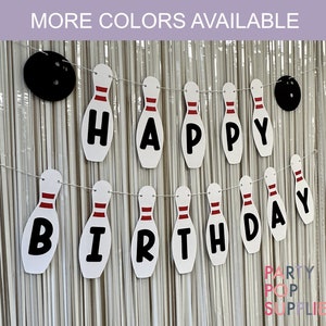 May include: White and red bowling pin shaped banner with the words "Happy Birthday" in black letters. The banner is strung with white twine and has black bowling balls on either end.