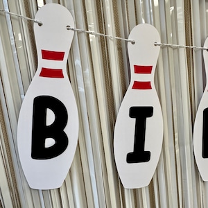 May include: White and red bowling pin shaped banner with the letters "BI" in black.