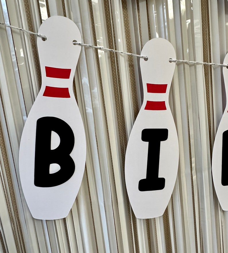 May include: White and red bowling pin shaped banner with the letters "BI" in black.