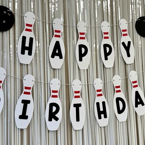 May include: White and red bowling pin shaped banner with the words "Happy Birthday" in black letters.