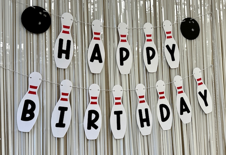 May include: White and red bowling pin shaped banner with the words "Happy Birthday" in black letters.