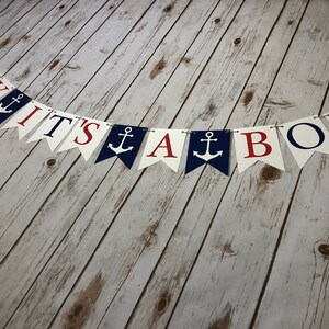Puede incluir: Una pancarta de Ahoy It's A Boy con banderines rojos, blancos y azules. Cada bander&iacute;n tiene una letra o un s&iacute;mbolo de ancla diferente. La pancarta est&aacute; enhebrada en una cuerda blanca.