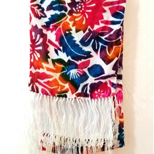 May include: A colorful scarf with a white background and a floral pattern. The scarf has a white fringe.