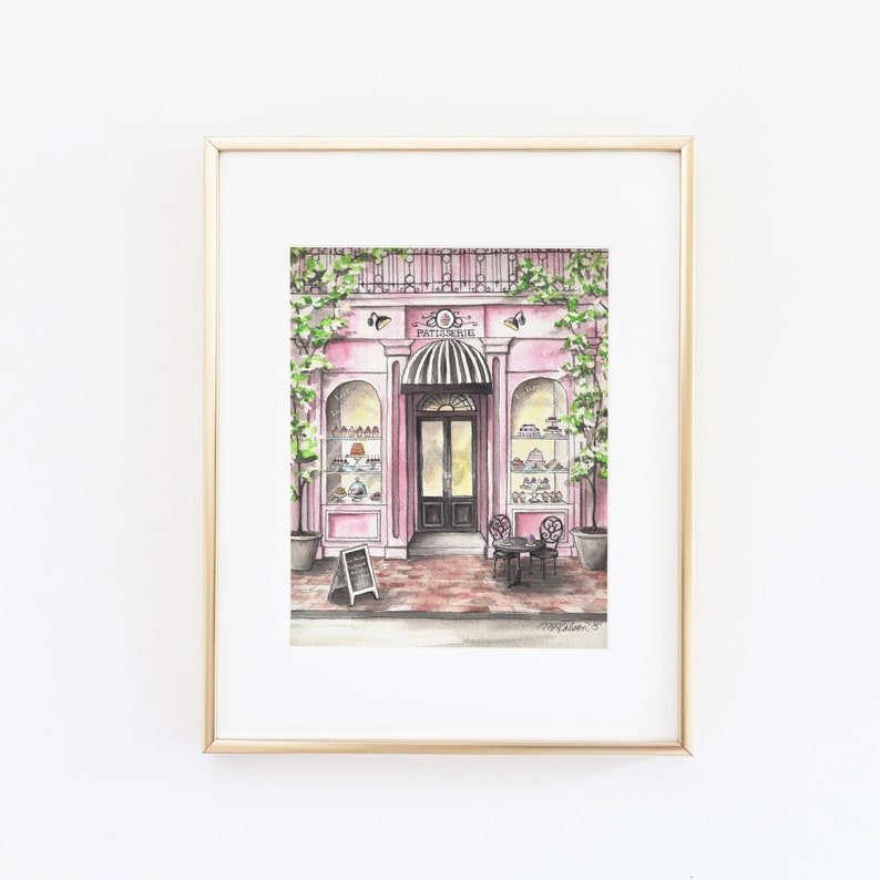 May include: A watercolor painting of a pink storefront with a sign that reads "Patisserie". The storefront has a glass display case filled with pastries and a black door with a striped awning. There is a table and chairs outside the store.