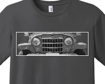 May include: Dark gray t-shirt featuring a black and white image of the front of a vintage Jeep. The image shows the headlights, grill, and bumper of the vehicle. The shirt has a crew neck and short sleeves.