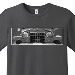 May include: Dark grey t-shirt with a black and white image of a vintage Jeep's front. The image shows the headlights, grille, and bumper. The shirt has a crew neck and short sleeves.