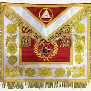 Puede incluir: Delantal masónico rojo con ribetes y bordados dorados. El delantal presenta un cuello blanco, un símbolo de compás y escuadra dorados y una corona con un cuadrado a cuadros en el centro.