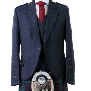 Può includere: Un kilt blu scuro con una giacca e un gilet abbinati. La giacca ha una cravatta rossa e uno sporran argentato.