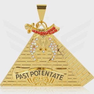 以下が含まれることがあります： 「PAST POTENTATE」の文字が入ったピラミッドデザインのゴールドトーンペンダント。ペンダントには、ピラミッドの上に赤とクリアの宝石がちりばめられたアクセントと、吊り下げ用のゴールドベイルが付いています。