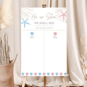 Op de afbeelding: Een wit bord op een houten ezel met de tekst "He or She, WE SHELL SEE!" in een scriptlettertype. Het bord heeft blauwe en roze zeester- en schelpgraphics, met ruimtes voor "BOY" en "GIRL" voorspellingen.