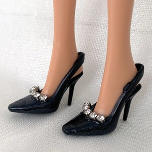 May include: A pair of black heeled shoes with a slingback design. The shoes have a pointed toe and are adorned with a row of clear rhinestones.