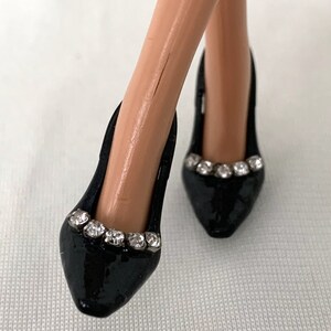 May include: A pair of black high-heeled shoes with a pointed toe and a row of rhinestones around the top of the shoe.