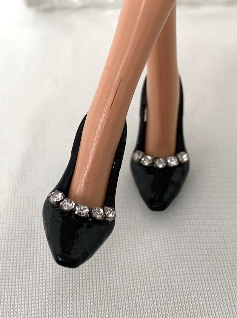 May include: A pair of black high-heeled shoes with a pointed toe and a row of rhinestones around the top of the shoe.