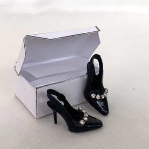 May include: A pair of black heeled shoes with a rhinestone embellishment on the strap, in a white box.