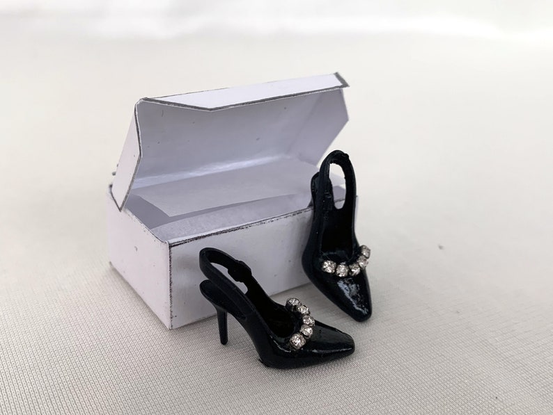 May include: A pair of black heeled shoes with a rhinestone embellishment on the strap, in a white box.