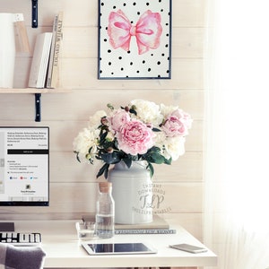 May include: A white desk with a computer, a vase of pink and white peonies, a glass of water, a cell phone, and a tablet. The vase has the text "Instant Downloads TLP The Lil Printables" on it. A framed print with a pink bow on a black and white polka dot background hangs on the wall behind the desk.