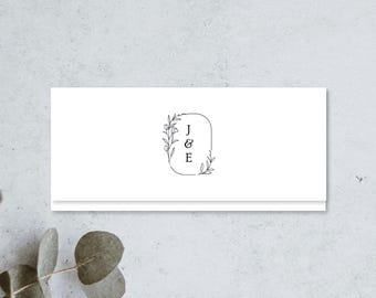 May include: A rectangular white card featuring a centered black line art logo. The logo consists of an oval frame partially surrounded by delicate floral stems and leaves, with the capital letters J, &, and E stacked vertically inside.