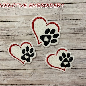 May include: Three embroidered patches in the shape of hearts with a paw print inside each heart. The hearts are white with a red outline and the paw prints are black with a white heart inside each paw print.