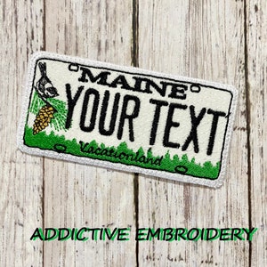 May include: White embroidered patch with a green pine tree, a small bird, and the text "MAINE YOUR TEXT Vacationland".