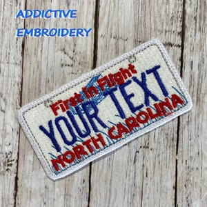 May include: White embroidered patch with a blue and red design. The patch says "First in Flight" and "YOUR TEXT" in blue and "NORTH CAROLINA" in red.