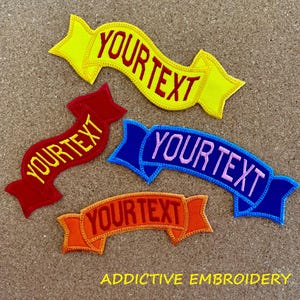 May include: Four embroidered iron-on patches in different colors, each with a curved banner design and the text "YOUR TEXT" in a contrasting color. The patches are on a brown corkboard background.