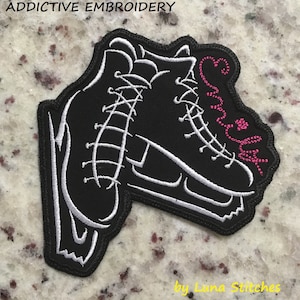 May include: Black and white embroidered patch of a pair of ice skates with the word "Snowflake" in pink lettering. The patch is made by Luna Stitches.