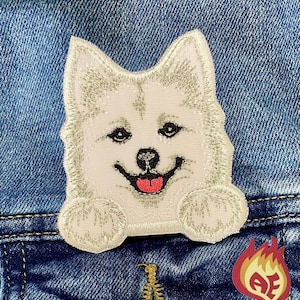 May include: Embroidered patch of a smiling white husky dog with gray accents, black eyes, and a pink tongue. The patch is on a blue denim background. A small, red and yellow patch with the letters "AE" is also visible.