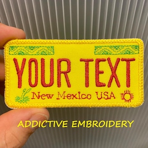 May include: Yellow embroidered patch with the text "YOUR TEXT" in red, above "New Mexico USA". The patch has a green border and a sun graphic. The text "ADDICTIVE EMBROIDERY" is below.