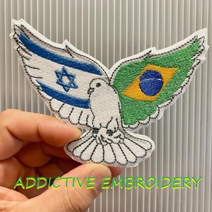 May include: Embroidered patch in the shape of a dove with wings featuring the flags of Israel and Brazil. The dove is white with black stitching, and the text "ADDICTIVE EMBROIDERY" is at the bottom in green.