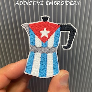 May include: Embroidered patch featuring a coffee maker design with a red top, a white star, and blue and white stripes. The handle is black. The text "ADDICTIVE EMBROIDERY" is at the top.