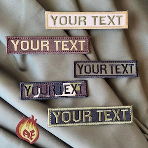 Op de afbeelding: Rechthoekige geborduurde patches met de tekst "YOUR TEXT" in verschillende kleuren, waaronder beige, bruin, groen en marineblauw. De patches worden getoond op een groene stoffen achtergrond. Een klein, vlamvormig logo staat linksonder.