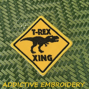 May include: Yellow diamond-shaped warning sign with a black embroidered T-Rex dinosaur and the text "T-Rex Xing".
