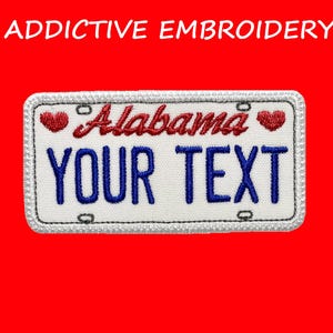 May include: Embroidered patch in the shape of an Alabama license plate. The patch features the word "Alabama" in red script, the text "YOUR TEXT" in blue block letters, and two red heart accents. The patch is bordered with white stitching and has the text "ADDICTIVE EMBROIDERY" at the top.