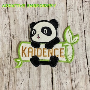 May include: Embroidered iron-on patch featuring a black and white panda bear holding onto a green bamboo shoot with the name "Kaidence" written in gold lettering.