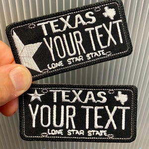 May include: Two black embroidered patches with white text. The patches read "TEXAS YOUR TEXT" and "LONE STAR STATE". One patch features a white star, the other a white outline of Texas. The patches are rectangular.