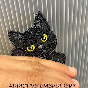 May include: Black cat embroidery patch with yellow eyes and the text "ADDICTIVE EMBROIDERY". The cat is peeking over an unseen object. The patch is made of black thread.