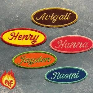 May include: Five oval-shaped embroidered patches featuring names in cursive script. The patches include a brown one with gold text reading Avigail, a yellow one with red text reading Henry, a pink one with red text reading Hanna, an orange one with green text reading Jayden, and a blue one with white text reading Naomi.