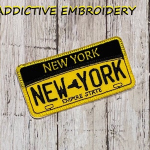 Op de afbeelding: Gele en zwarte geborduurde patch met de tekst "NEW YORK" en "EMPIRE STATE" op een houten achtergrond.