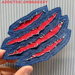 May include: A red fabric patch with a blue denim border. The denim is cut into strips and frayed, creating a distressed look. The patch is shaped like a claw.