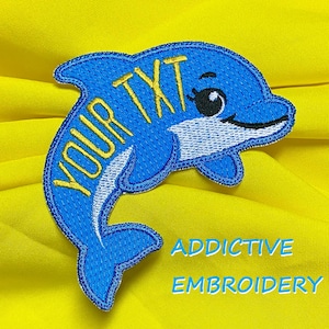 Puede incluir: Parche de delfín azul bordado con el texto "YOUR TXT" en amarillo. El parche tiene una barriga blanca y un ojo negro. Las palabras "ADDICTIVE EMBROIDERY" están debajo del delfín sobre un fondo amarillo.