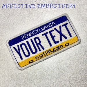 May include: White embroidered patch with a blue and yellow Pennsylvania license plate design. The plate says "PENNSYLVANIA" at the top and "YOUR TEXT" in the centre. The bottom of the plate says "visitPA.com".