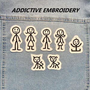 Peut inclure: Écussons brodés représentant des familles et des animaux de compagnie en forme de bonhommes allumettes. Les écussons sont blancs avec des contours noirs, disposés sur une veste en jean. Le texte "ADDICTIVE EMBROIDERY" est au-dessus.