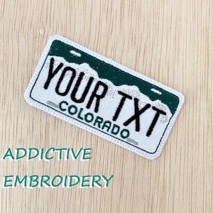 May include: White embroidered patch with a green mountain design and the text "YOUR TXT" and "COLORADO" in black.
