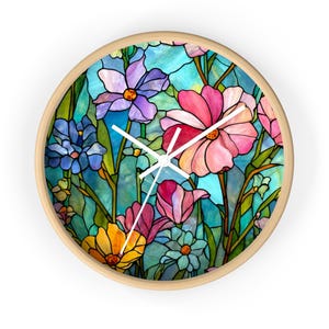Könnte beinhalten: Runde Wanduhr mit hellem Holzrahmen. Das Zifferblatt zeigt ein farbenfrohes Buntglasdesign mit Blumen in Rosa, Lila, Blau und Gelb vor einem türkisfarbenen Hintergrund. Weiße Zeiger zeigen die Uhrzeit an.